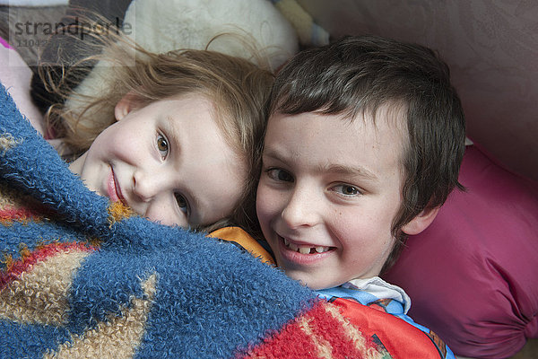 Junge Geschwister liegen zusammen unter der Decke  Porträt