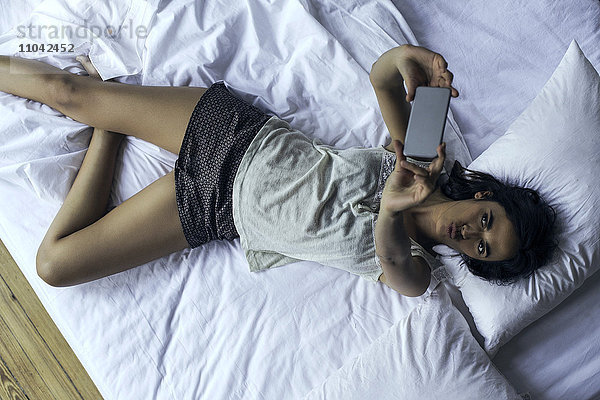 Frau  die auf dem Bett liegt und Selfie mit Smartphone nimmt