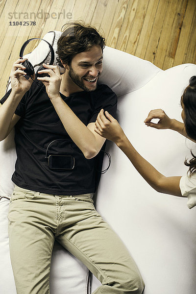 Mann hält spielerisch Kopfhörer von Freundin fern