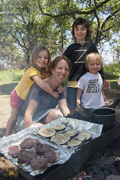 Mutter und Kinder beim gemeinsamen Grillen auf dem Campingplatz