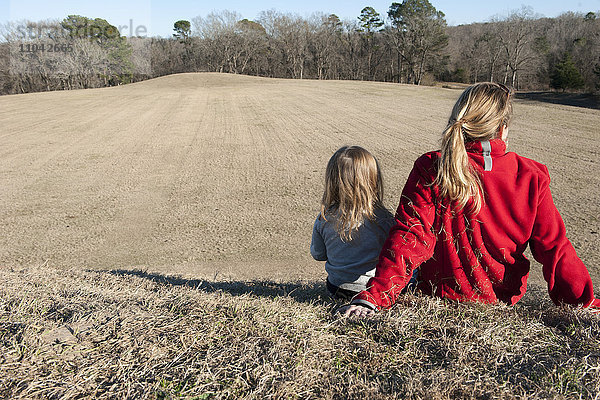 Mutter und Tochter sitzen zusammen auf einem Hügel  Rückansicht