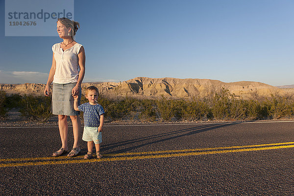 Mutter und Kleinkind gehen gemeinsam auf gepflasterter Straße durch die Wüste