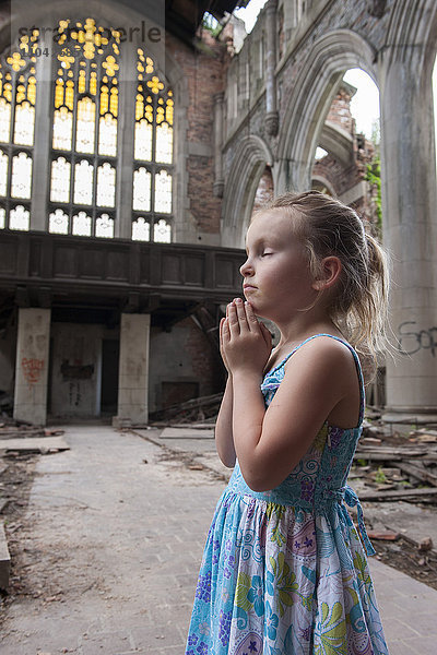 Kleines Mädchen betet in der zerstörten Kirche