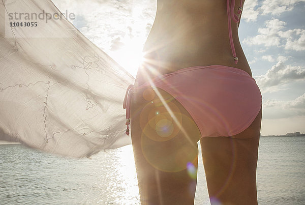 Kaukasische Frau im Bikini hält Stoff am Strand