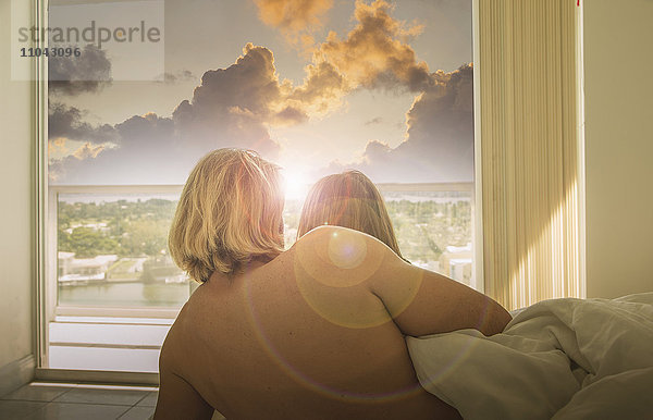 Kaukasisches Paar im Bett beobachtet Sonnenuntergang am Fenster