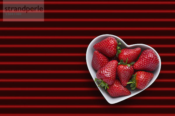 Erdbeeren in herzförmiger Schale auf rot gestreiftem Hintergrund