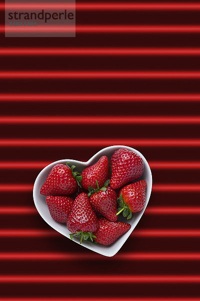 Erdbeeren in herzförmiger Schale auf rot gestreiftem Hintergrund