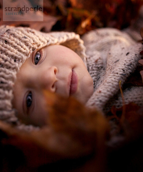 Nahaufnahme eines kleinen Jungen  der im Herbstlaub liegt