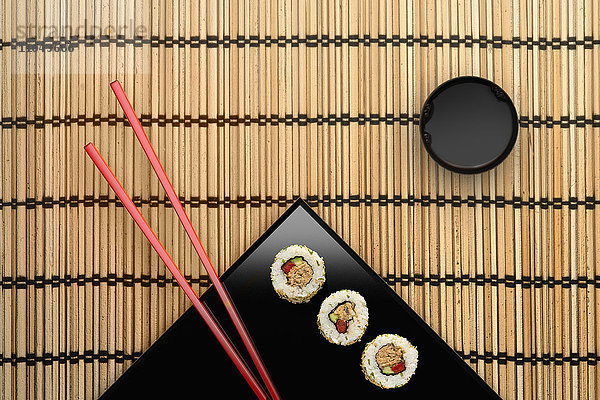 Stäbchen und Sushi auf quadratischem Teller mit Dip-Sauce