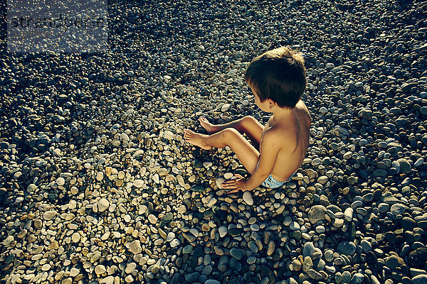 Hoher Blickwinkel auf einen Jungen  der am felsigen Strand sitzt