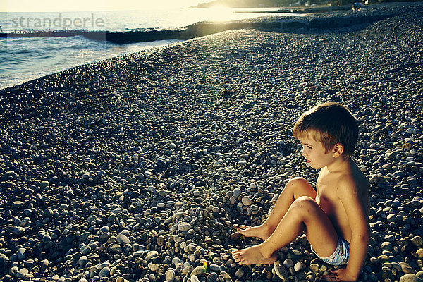 Hoher Blickwinkel auf einen Jungen  der am felsigen Strand sitzt