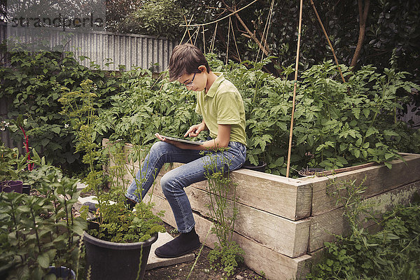 Gemischtrassiger Junge benutzt digitales Tablet im Garten