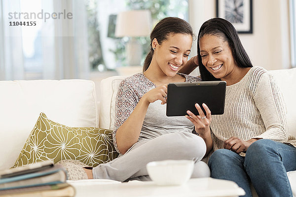 Mutter und Tochter benutzen ein digitales Tablet auf dem Sofa