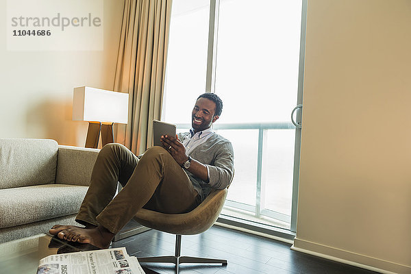 Schwarzer Mann benutzt digitales Tablet im Wohnzimmer