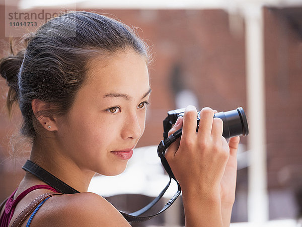 Gemischtrassiges Mädchen beim Fotografieren im Freien mit Digitalkamera