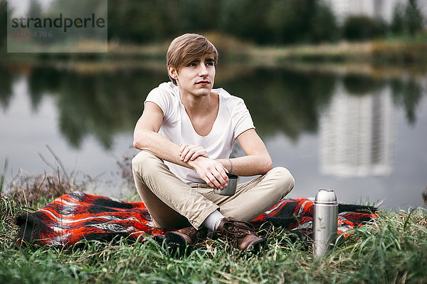 Kaukasischer Mann sitzt in der Nähe eines ländlichen Teichs
