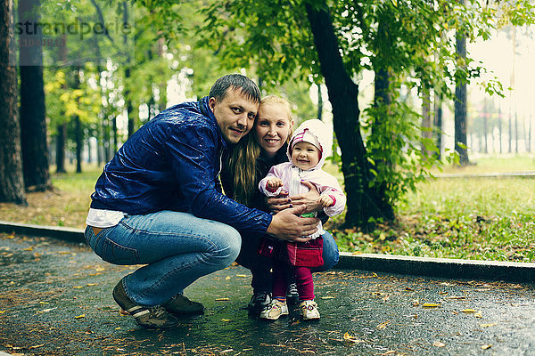Kaukasische Familie lächelnd auf regnerischem Weg im Park