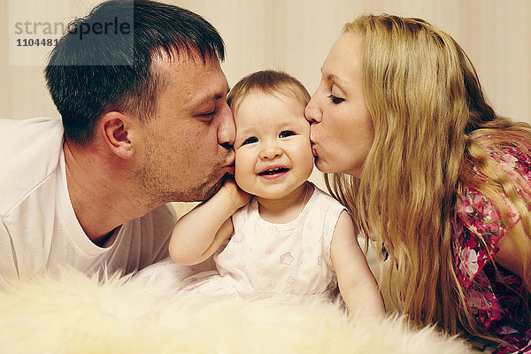 Kaukasische Eltern  die ihre kleine Tochter im Bett küssen