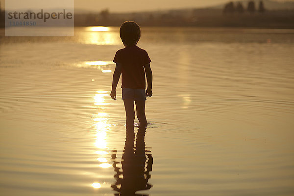 Silhouette eines im Teich stehenden Jungen bei Sonnenuntergang