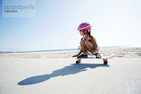 Gemischtrassiges Mädchen fährt Skateboard am Strand