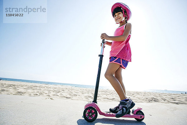 Gemischtrassiges Mädchen fährt Roller am Strand