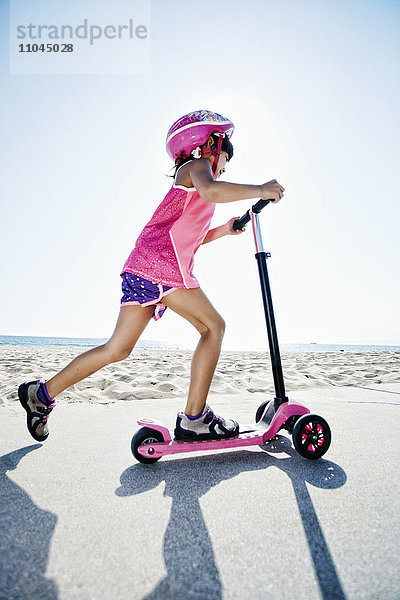 Gemischtrassiges Mädchen fährt Roller am Strand