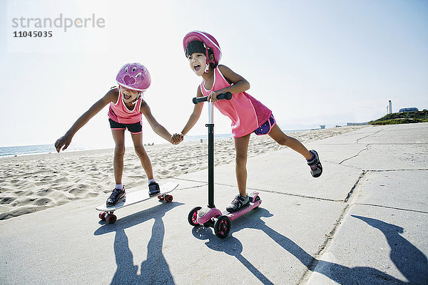 Mädchen fahren Skateboard und Roller am Strand