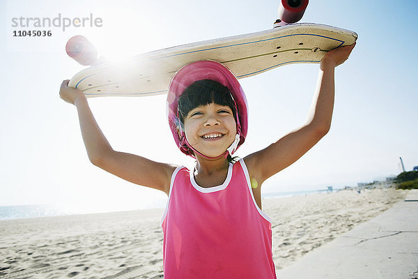 Gemischtrassiges Mädchen hält Skateboard am Strand
