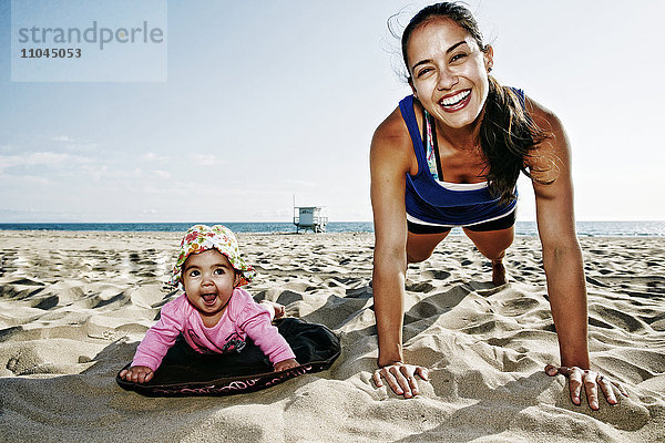 Mutter und Tochter machen Liegestütze am Strand