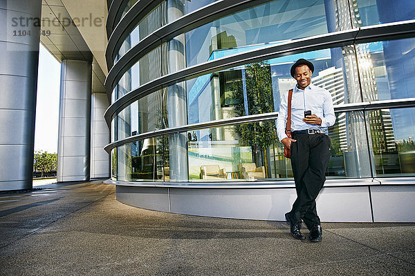 Schwarzer Geschäftsmann benutzt Mobiltelefon vor Bürogebäude