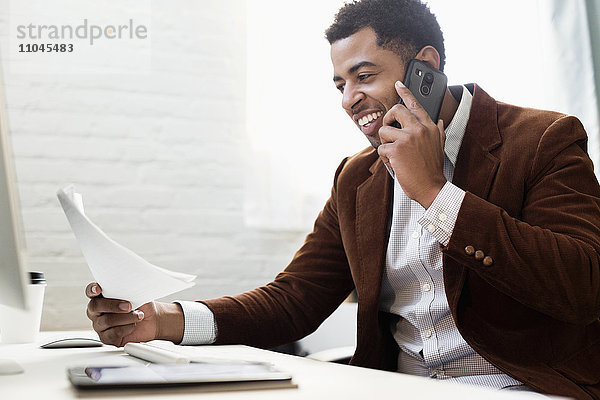 Afroamerikanischer Geschäftsmann  der im Büro mit seinem Handy telefoniert