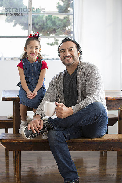 Hispanischer Vater und Tochter lächelnd am Tisch