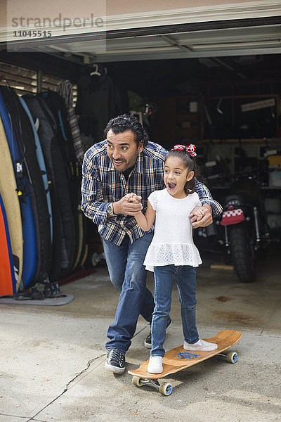 Hispanischer Vater bringt seiner Tochter das Skateboardfahren bei