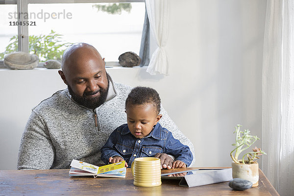 Afroamerikanischer Vater und Sohn lesen ein Buch am Tisch