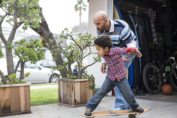 Gemischtrassiger Vater bringt seinem Sohn das Skateboardfahren im Freien bei