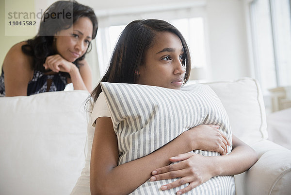 Mutter beobachtet nachdenkliche Tochter  die sich an ein Kissen klammert