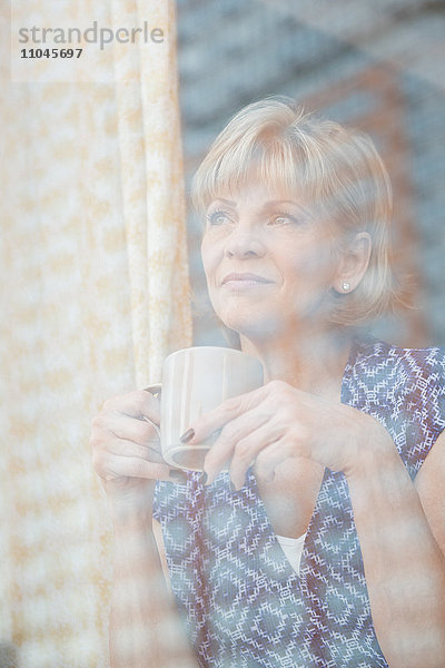 Ältere kaukasische Frau trinkt Kaffee am Fenster