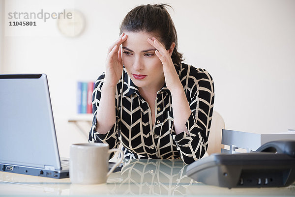 Kaukasische Geschäftsfrau mit Kopfschmerzen am Laptop
