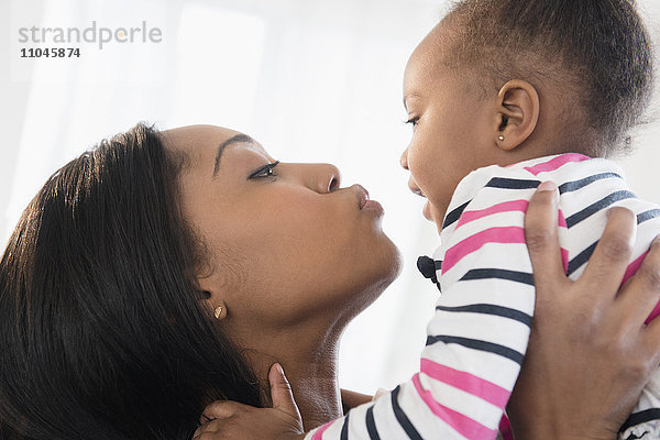 Schwarze Mutter hebt ihre kleine Tochter von Angesicht zu Angesicht