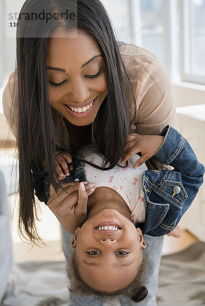 Schwarze Mutter hält ihre kleine Tochter verkehrt herum