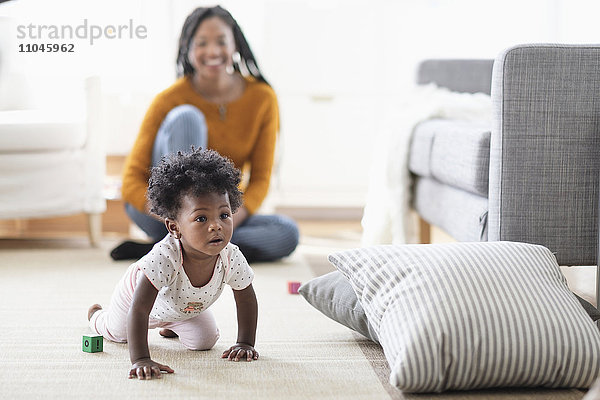 Schwarze Frau beobachtet  wie ihre kleine Tochter zum Kopfkissen krabbelt