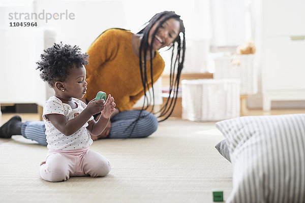 Schwarze Frau beobachtet Baby Tochter spielen mit Spielzeug auf Teppich