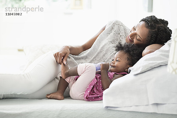 Schwarze Frau spielt mit dem Fuß ihrer kleinen Tochter auf dem Bett
