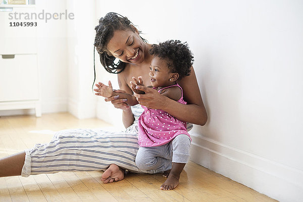 Schwarze Frau sitzt auf dem Boden und küsst klatschende Hände mit Baby-Tochter
