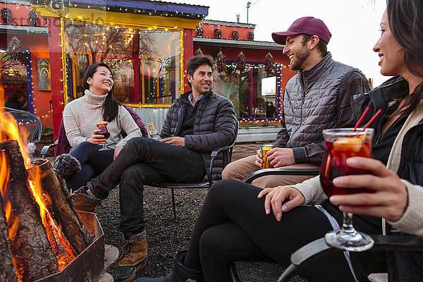 Paare trinken Cocktails und Bier im Freien am Lagerfeuer vor dem Geschäft