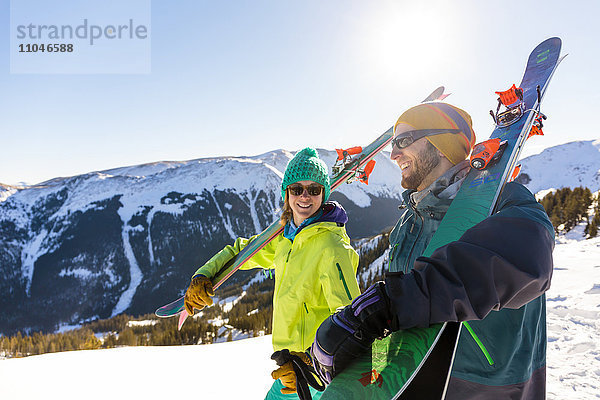 Paar trägt Skier auf verschneitem Berg