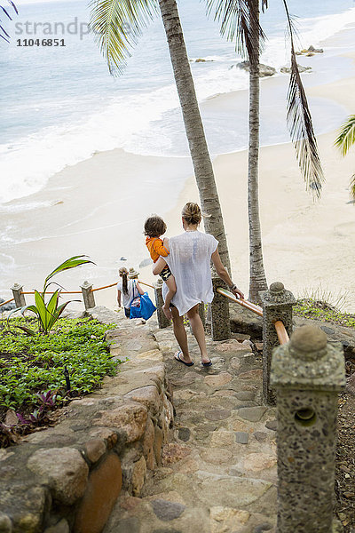 Kaukasische Mutter trägt ihren Sohn die Treppe zum Strand hinunter