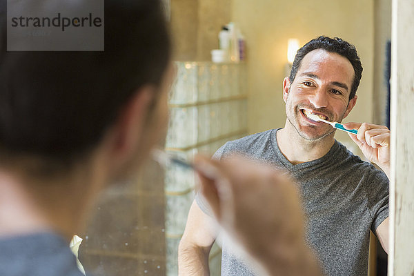 Hispanischer Mann beim Zähneputzen im Spiegel