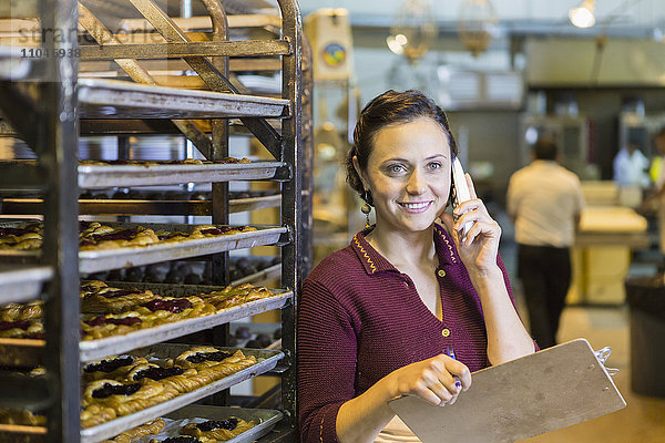 Kaukasische Frau mit Klemmbrett und Telefon in einer Bäckerei