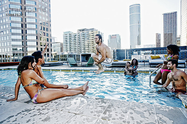 Freunde beobachten einen Mann  der mit einer Kanonenkugel in ein städtisches Schwimmbad springt